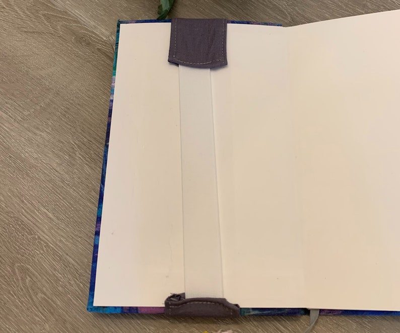 May include: A blue and purple patterned notebook with a white elastic closure and a grey fabric bookmark.