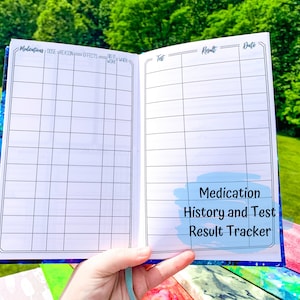 Peut inclure: Carnet ouvert avec un motif galaxie bleu et violet. Les pages int&eacute;rieures sont blanches avec des lignes de grille noires et des titres pour suivre les m&eacute;dicaments et les r&eacute;sultats des tests. Le texte "Medication History and Test Result Tracker" est visible.