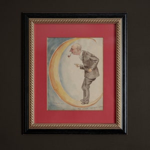 Puede incluir: Una pintura al agua enmarcada de un hombre con traje de pie sobre una luna creciente. El hombre sostiene una pipa en la boca y señala con la mano derecha. La pintura está titulada "El artista" y firmada por el artista.