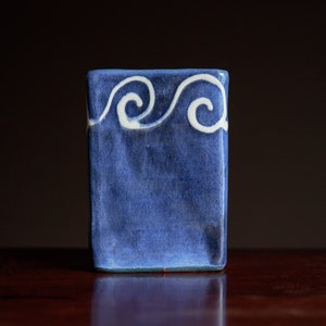 May include: A small, square, blue ceramic tile with a white wave design.