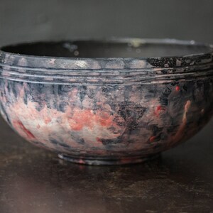 May include: A black ceramic bowl with a red and white marbled glaze. The bowl has a slightly rounded shape and a smooth, glossy finish.