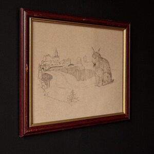 May include: Framed pencil sketch of a lynx and a European castle scene. The artwork is in a dark red wooden frame with a gold inner border. The drawing is on tan paper, and the lynx is seated.
