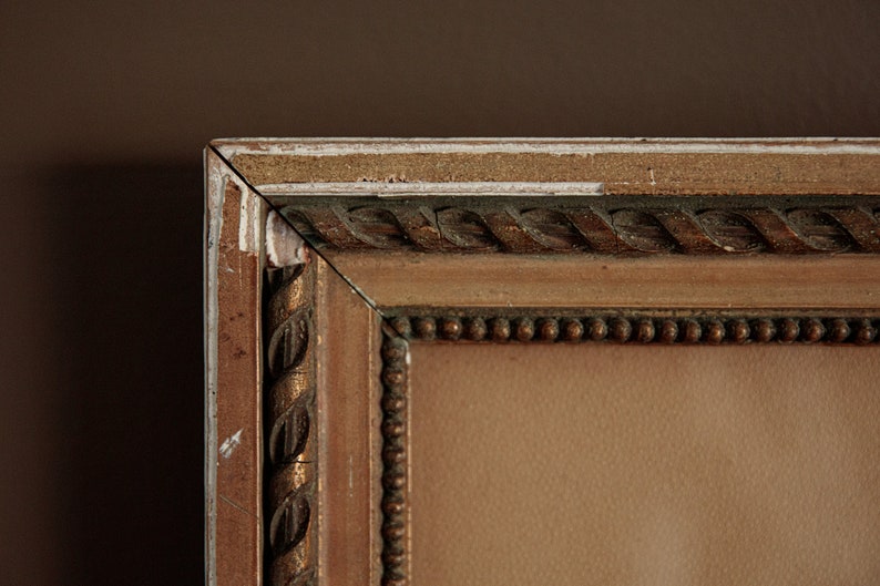 Pode incluir: Close-up do canto superior de uma moldura de madeira marrom com detalhes dourados e uma borda de contas. A moldura est&aacute; ligeiramente desgastada com tinta branca aparecendo.