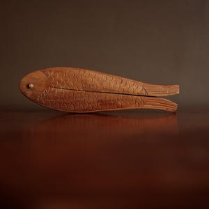 May include: A wooden nutcracker shaped like a fish. The nutcracker is brown and has a carved design.