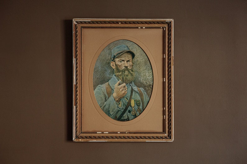 Pode incluir: Um retrato emoldurado de um homem em uniforme militar, com barba e bigode, segurando um cachimbo na m&atilde;o direita. O retrato est&aacute; sobre um fundo marrom claro.
