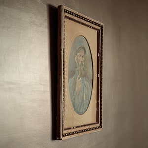 Pode incluir: Um retrato emoldurado de um homem com barba usando um bon&eacute; e uma camisa azul. A moldura &eacute; ornamentada e tem um acabamento dourado.