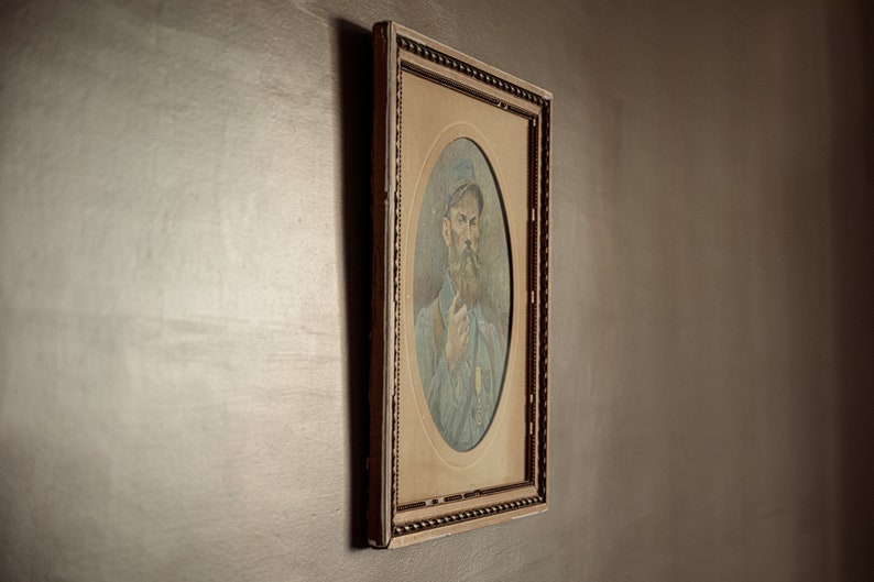 Pode incluir: Um retrato emoldurado de um homem com barba usando um bon&eacute; e uma camisa azul. A moldura &eacute; ornamentada e tem um acabamento dourado.