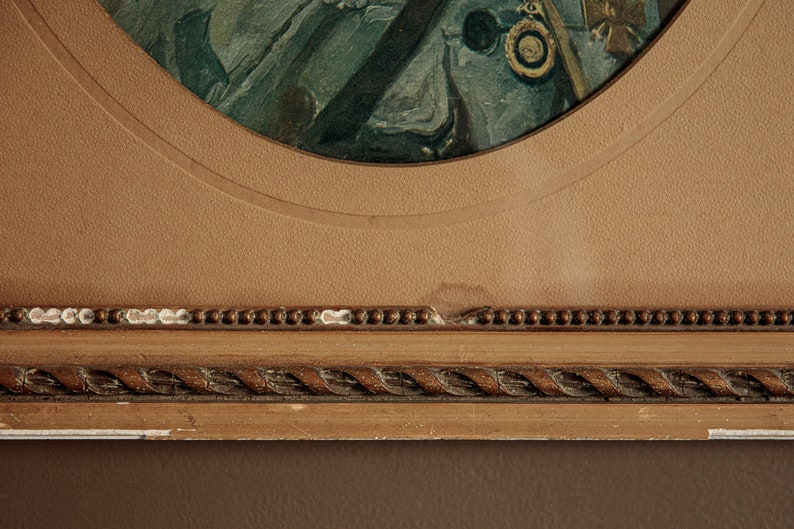 Pode incluir: Um close-up de uma moldura de imagem de madeira marrom com um design de corda ao redor da borda. A moldura tem um passe-partout marrom claro com uma abertura circular. O passe-partout tem uma pequena mancha branca na borda inferior.