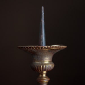 Puede incluir: Un candelero de lat&oacute;n vintage con un portavelas de metal puntiagudo. El candelero tiene una base decorativa y estriada.