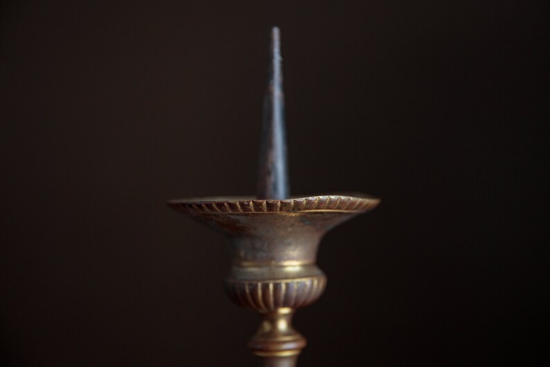 Puede incluir: Un candelero de lat&oacute;n vintage con un portavelas de metal puntiagudo. El candelero tiene una base decorativa y estriada.