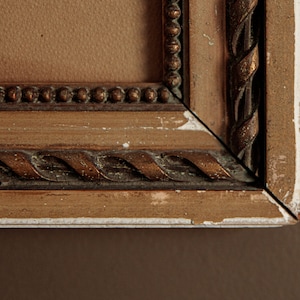 Pode incluir: Close-up de um canto de uma moldura de imagem de madeira com uma moldura dourada e um design de corda. A moldura est&aacute; ligeiramente desgastada, com alguma tinta branca aparecendo.