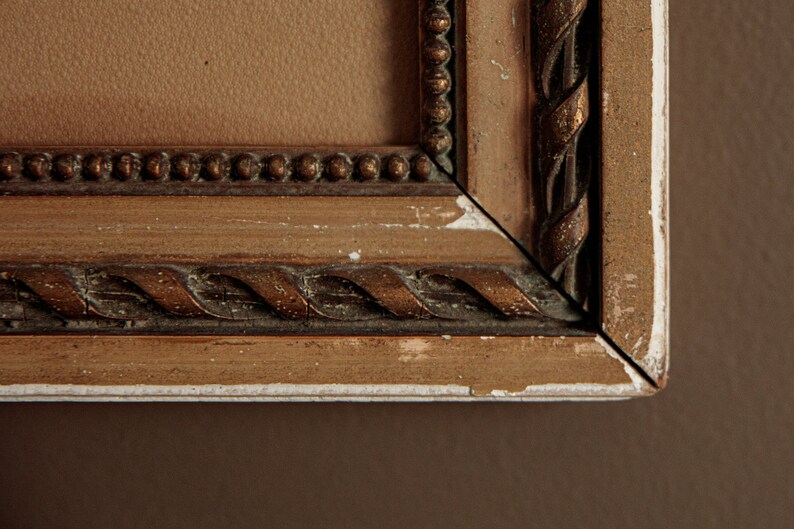 Pode incluir: Close-up de um canto de uma moldura de imagem de madeira com uma moldura dourada e um design de corda. A moldura est&aacute; ligeiramente desgastada, com alguma tinta branca aparecendo.
