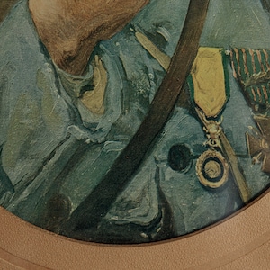 Pode incluir: Close-up de um uniforme militar com uma medalha verde e dourada e uma correia marrom. O uniforme &eacute; azul escuro e a medalha tem uma fita vermelha e branca.