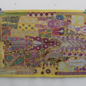 以下が含まれることがあります： カラフルな刺繍の花柄と幾何学模様が施された黄色のパッチワークの壁掛けです。