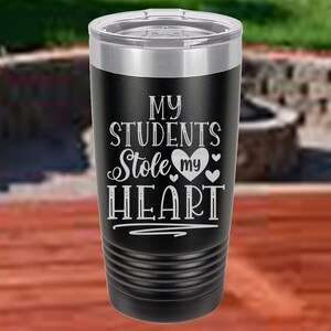 May include: Black stainless steel tumbler with a white inscription that reads "My Students Stole My Heart" with a heart and smaller hearts around it.