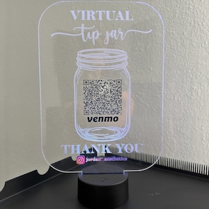 May include: A clear acrylic sign with rounded corners featuring the white text VIRTUAL tip jar, a mason jar graphic with a QR code, the word venmo, the text THANK YOU, and an Instagram icon with the handle jordan_aesthetics on a black base.
