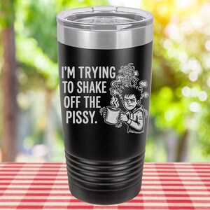 May include: Black insulated tumbler with a silver rim and lid. The tumbler features the text "I'M TRYING TO SHAKE OFF THE PISSY." along with a graphic of a person holding a mug and looking disgruntled. The tumbler is cylindrical and has a ridged design.
