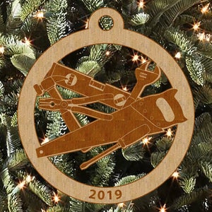 May include: A wooden Christmas ornament shaped like a circle with a brown saw, wrench, pliers, and level inside. The ornament has the year 2019 printed on the bottom.