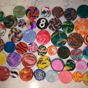 May include: A collection of 38 colourful, round, swirl-patterned clay coasters. The coasters are arranged in a semi-circle pattern on a white surface. The number "8" is written in black on a white circle in the centre of the arrangement.