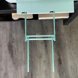 May include: A set of two teal metal shelf brackets, extending down from a shelf, with a horizontal bar connecting the two brackets.