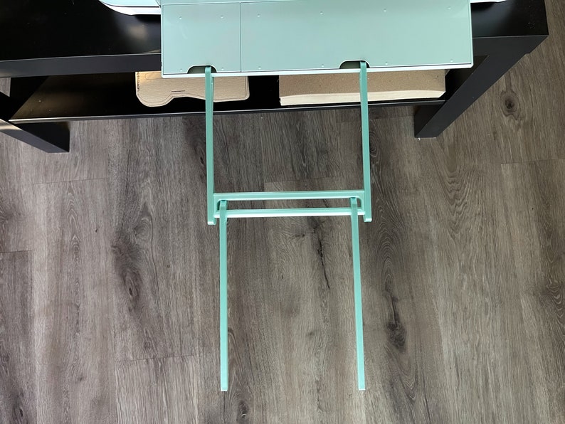 May include: A set of two teal metal shelf brackets, extending down from a shelf, with a horizontal bar connecting the two brackets.