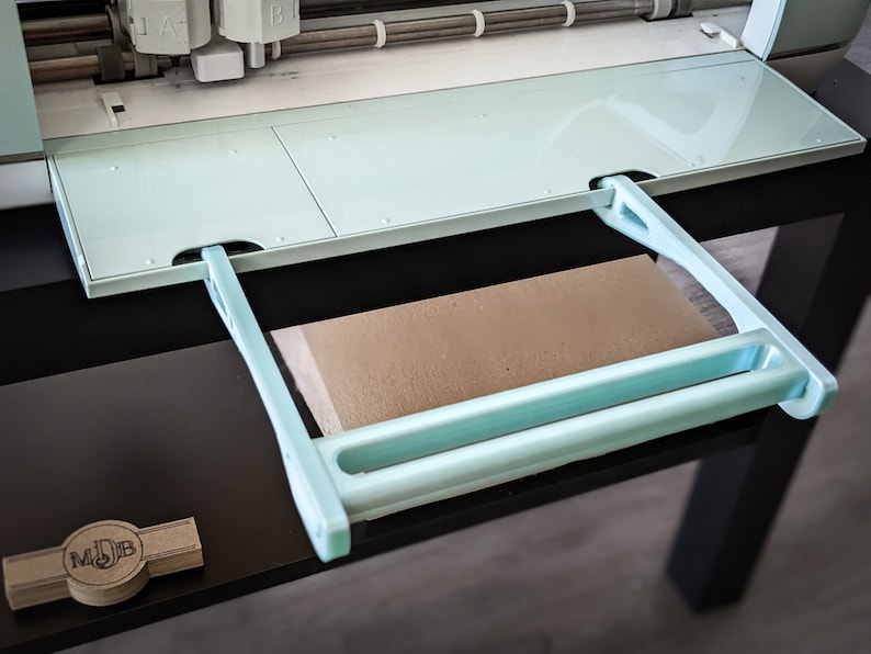 May include: A light blue cutting machine with a retractable extension platform. The platform is made of plastic and has a light blue handle. The machine is sitting on a black surface.