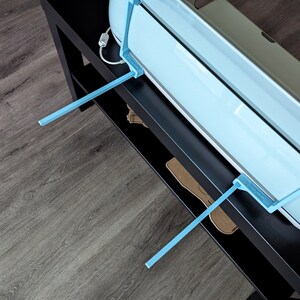 May include: A light blue vinyl cutter with two blue support arms, sitting on a black surface.
