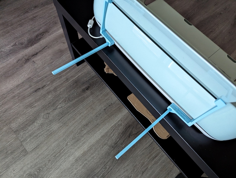 May include: A light blue vinyl cutter with two blue support arms, sitting on a black surface.