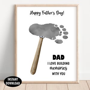 May include: A framed print featuring the text Happy Father's Day! at the top and DAD I LOVE BUILDING MEMORIES WITH YOU at the bottom. In the center is a gray watercolor footprint shaped like a hammer head with a brown wooden handle attached.