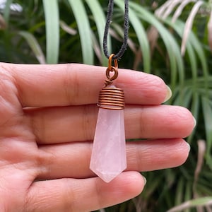 May include: A pink rose quartz crystal pendant with a copper wire wrap, hanging from a black cord.