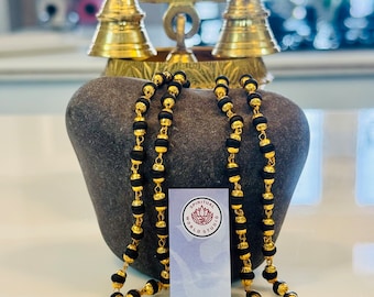 May include: A black beaded mala necklace with gold accents. The necklace is draped over a grey stone and a small white card with the text "Spiritual World Studio".