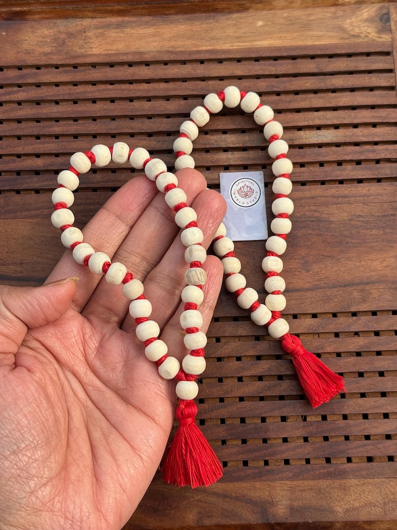 May include: A white and red prayer beads mala with a tassel on each end. The beads are made of wood and are strung together with red thread.
