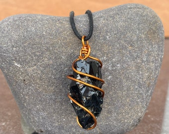 May include: Black obsidian stone pendant wrapped in copper wire, hanging from a black cord.