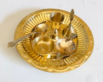 May include: A gold metal plate with a decorative design, containing a small gold spoon, a small gold bowl, a small gold cup, a small gold incense burner, and a small gold bell.