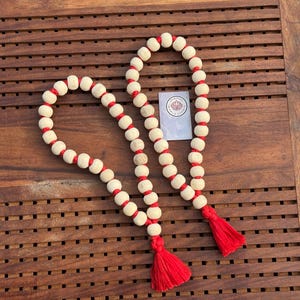 May include: Two wooden bead necklaces with red tassels. The beads are white with red string accents.