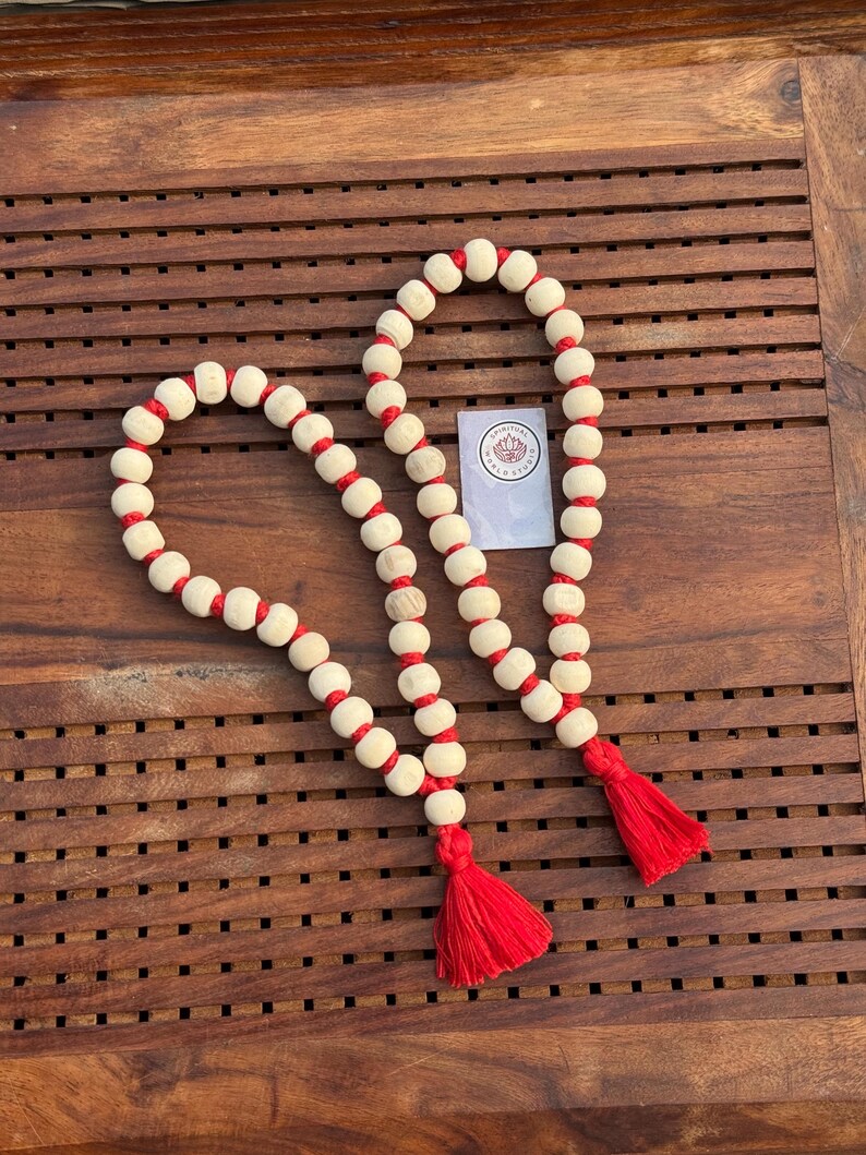May include: Two wooden bead necklaces with red tassels. The beads are white with red string accents.
