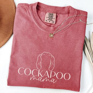 May include: A red t-shirt with a white outline of a cockapoo dog and the text "Cockapoo mama".