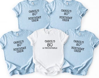 May include: Five t-shirts, four light blue and one white, with black text. The light blue shirts read "Carol's 80th Birthday Crew." The white shirt says "Carol's 80 & Unstoppable."