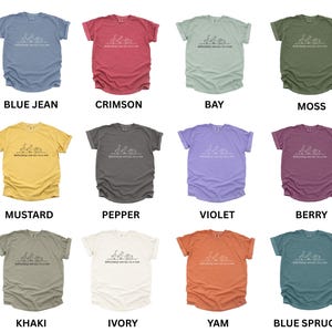 May include: A collection of twelve t-shirts in various colors, including blue jean, crimson, bay, moss, mustard, pepper, violet, berry, khaki, ivory, yam, and blue spruce. Each shirt features a white graphic and the text "Definitely not all a row."