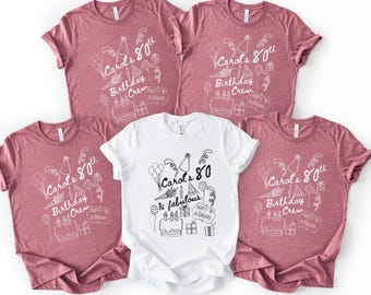 May include: Five t-shirts, four in a dusty rose color and one in white. Each shirt features the text "Carol's 80th Birthday Crew" with celebratory doodles. The white shirt says "Carol's 80 & fabulous".