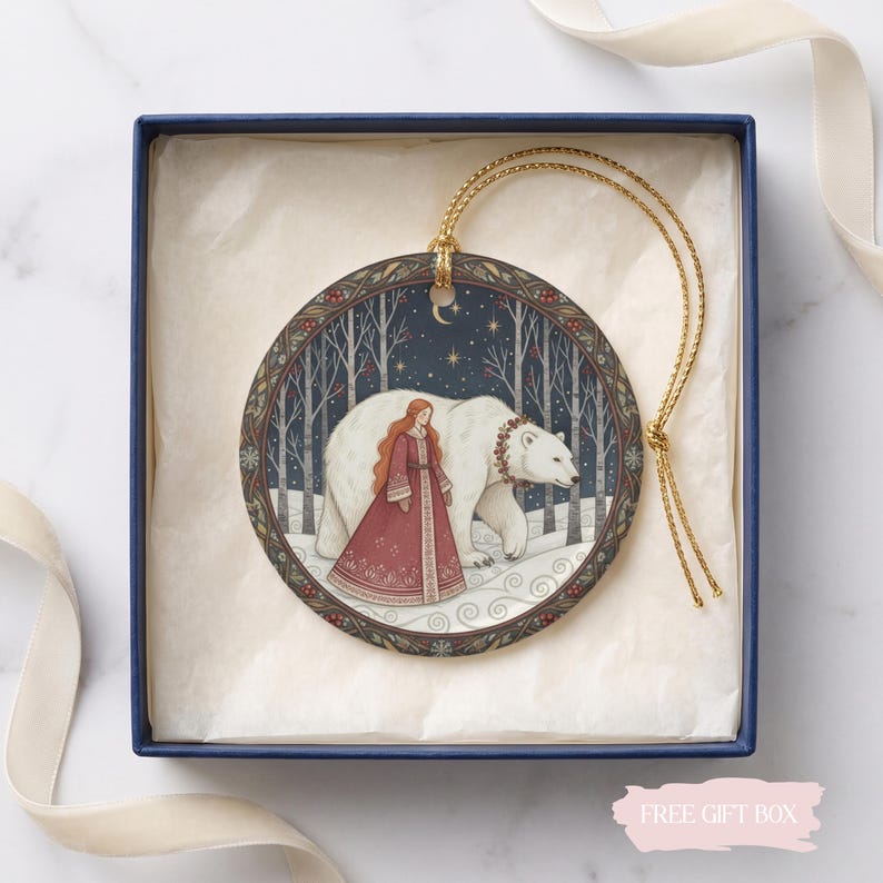 May include: A round ceramic ornament featuring an illustration of a person with long red hair in a maroon dress standing next to a large white polar bear in a snowy forest with bare trees, stars, and a crescent moon, finished with a gold cord.