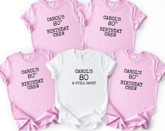 May include: Five t-shirts, four pink and one white, with black text. The pink shirts read "CAROL'S 80TH BIRTHDAY CREW." The white shirt says "CAROL'S 80 & STILL SASSY."