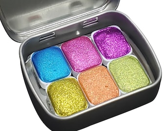 May include: A silver metal tin with six small pans of glitter paint. The pans are arranged in two rows of three. The colors are blue, pink, green, yellow, orange, and purple.