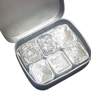 K&ouml;nnte beinhalten: Eine silberne Metalldose mit sechs silbernen Aquarellfarben-Pans. Die Dose ist ge&ouml;ffnet und die Farb-Pans sind sichtbar.