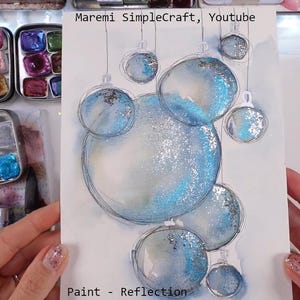 K&ouml;nnte beinhalten: Ein Aquarellbild von blauen und silbernen Weihnachtskugeln mit Glitzer. Das Bild ist auf wei&szlig;em Hintergrund und hat den Text "Paint - Reflection" unten.