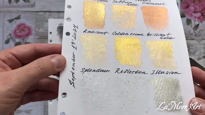 May include: A white card with swatches of gold paint. The swatches are labeled "Theol. 67 squs", "Saftrefold", "Caramel", "Radiant", "Golden crown", "Brilliant Gold", "Splendour", "Reflection", and "Illusion". The card also has the text "September 19' 10:34" written on it.