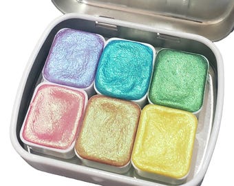 May include: A tin of six iridescent watercolor paints in a rainbow of colors, including pink, yellow, green, blue, and purple.