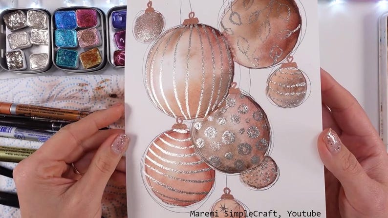 K&ouml;nnte beinhalten: Ein Aquarellbild von Weihnachtskugeln mit silbernem Glitzerfinish. Die Kugeln sind in Braun- und Rosat&ouml;nen bemalt und h&auml;ngen an F&auml;den. Das Bild ist signiert mit "Maremi SimpleCraft, Youtube".