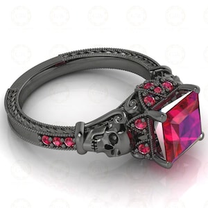 May include: Black ring with a large square red gemstone and a skull design. The ring is adorned with smaller red gemstones.