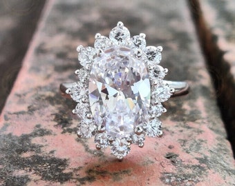 May include: A silver ring with a large oval-shaped clear gemstone surrounded by a halo of smaller clear gemstones.